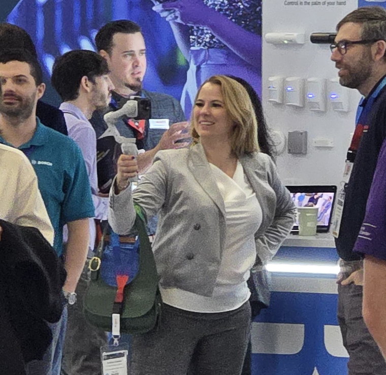 Barbara Zelenay on a trade show floor holding a phone on a gimbal up to film, surrounded by visitors at a Bosch stand.