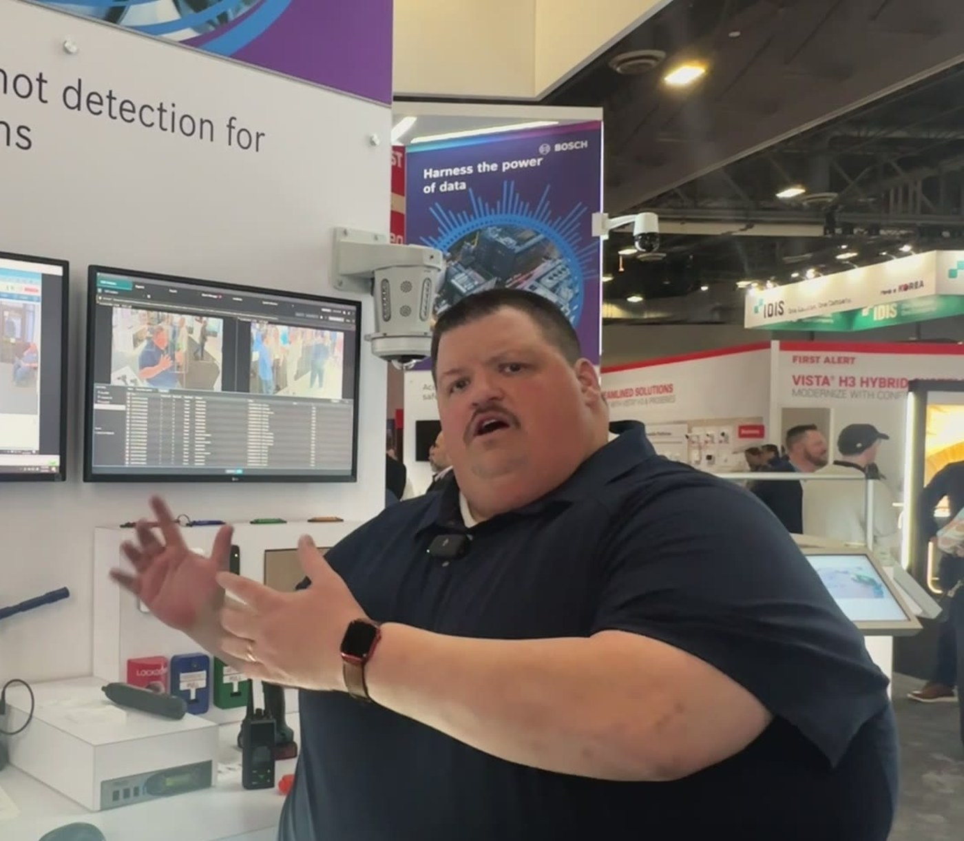 Kevin Kosch mid-sentence at the Bosch booth, gesturing with both hands, a clip mic on his collar.